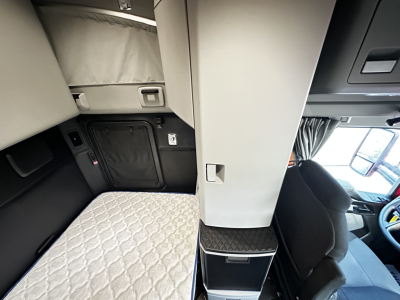 Kenworth T680 truck cab interior showing sleeper area with quilted mattress, side storage, and driver's seat; central partition and dashboard visible.