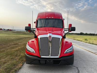Kenworth T680 front view in red with large chrome grille, side mirrors, and sleeper cab, daytime outdoor setting.
