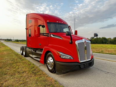 Kenworth T680 tractor trailer in red, front three-quarter view on road, large chrome grille, dual headlights, black bumper and fenders.