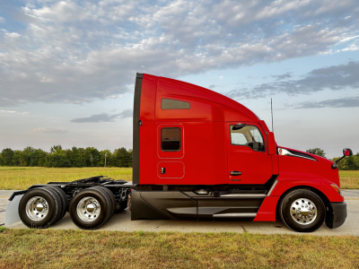 Side view of red Kenworth T680 sleeper cab tractor with tri-axle rear, showing smooth body lines and chrome wheels.
