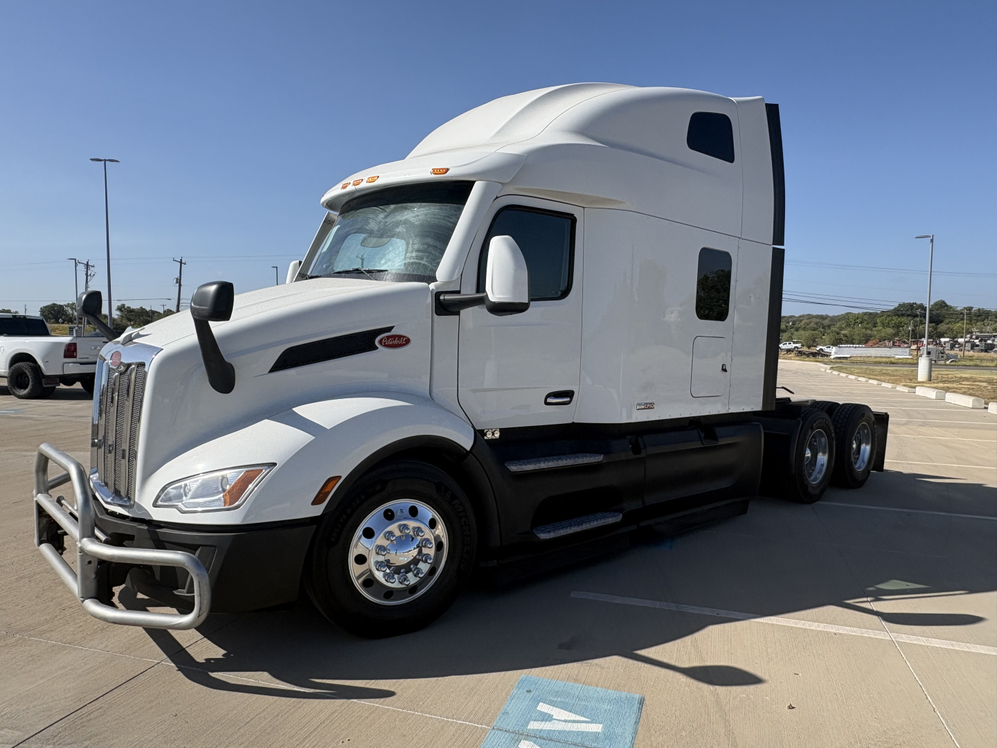 Peterbilt 579 conventional sleeper truck in white, side view showing front bumper guard, dual rear axles, and cab with aerodynamic features.