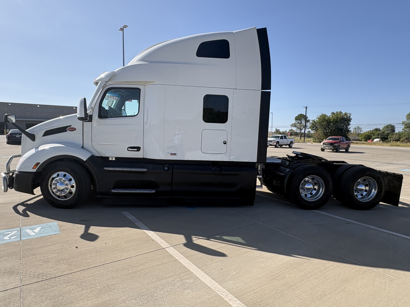 Peterbilt 579 tractor in side profile with white cab and black lower trim, no trailer attached, parking lot in background.