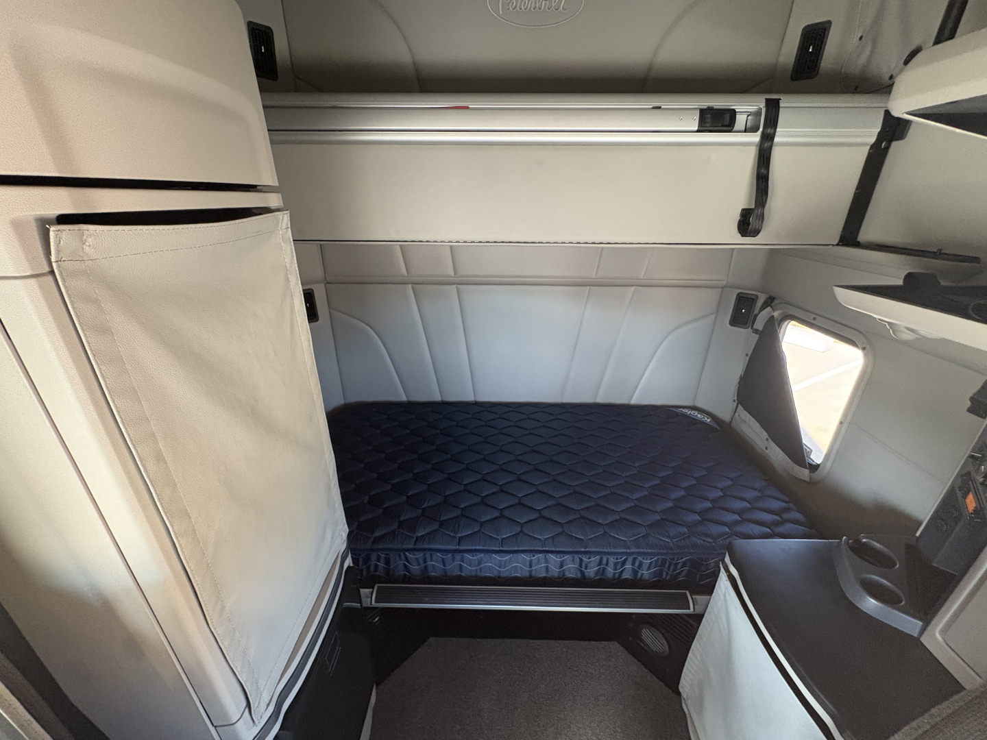 Peterbilt 579 sleeper cab interior showing bunk bed with quilted mattress and storage compartments.