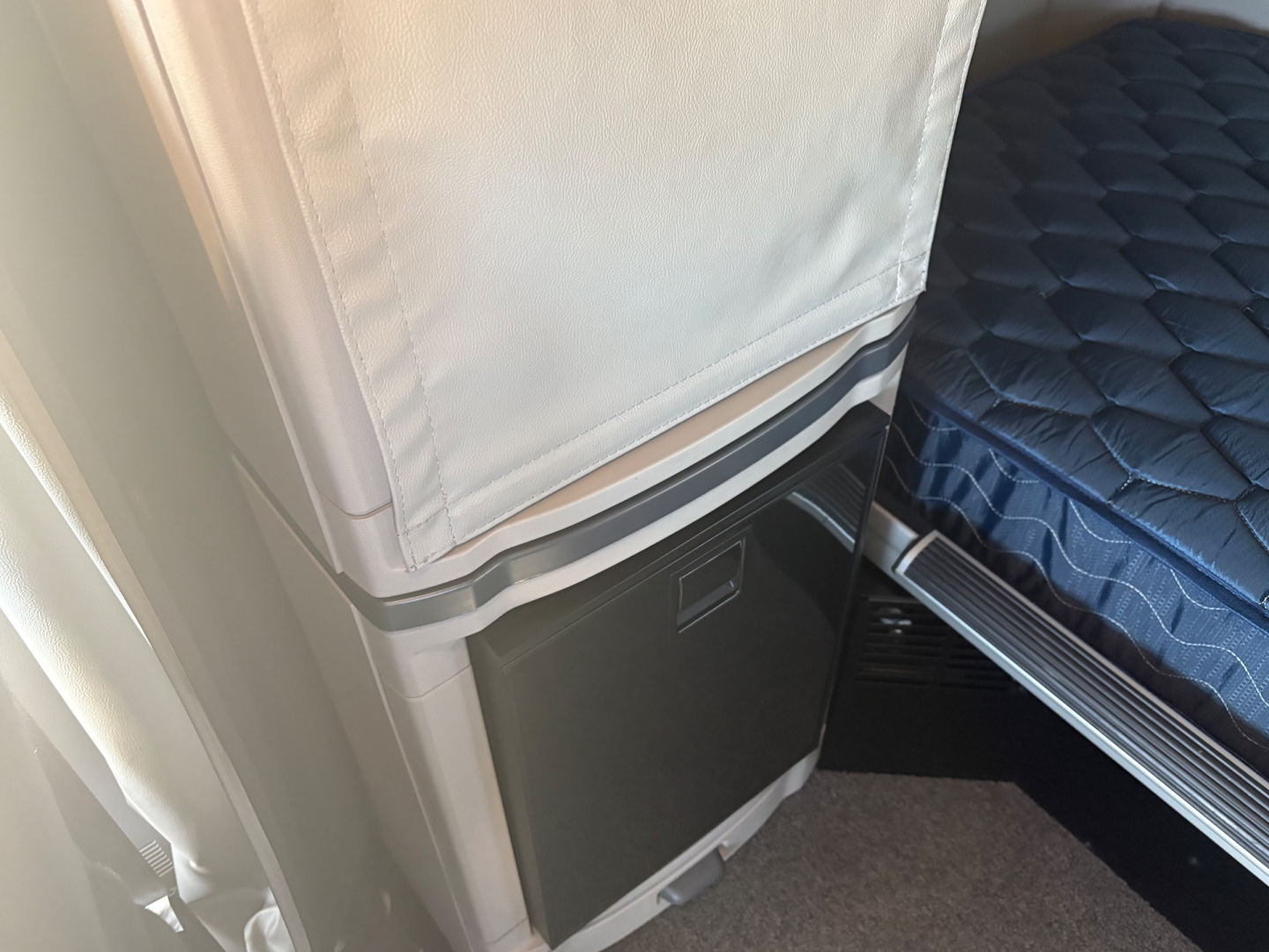Peterbilt 579 sleeper cab interior area with refrigerated unit and bed, showing storage cabinet and mattress edge.