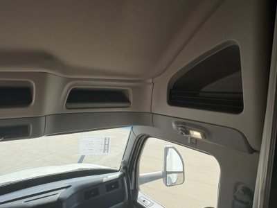 Trucks cab interior view of a Peterbilt 579, dashboard area with overhead storage, lighted reading lamps, and passenger door window visible.