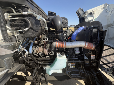 Peterbilt 579 engine bay showing coolant reservoir and intake piping in a used truck with blue silicon hose and orange sleeve clamps.