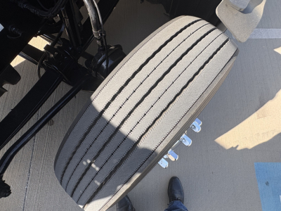 Truck front tire/wheel assembly on a Peterbilt 579 chassis showing tread marks and dual front axle details with chrome lug nuts.