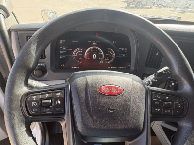 Peterbilt steering wheel and digital instrument cluster in cab showing gauges and controls. Visible on dash: Peterbilt logo on steering wheel, multiple control buttons, digital speedometer and tachometer readouts.
