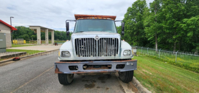 Front view of a white 2002 International DT530 dump truck showing grille, bumper, and headlights. The truck has a brown dump body hinge area visible and a clear windshield.