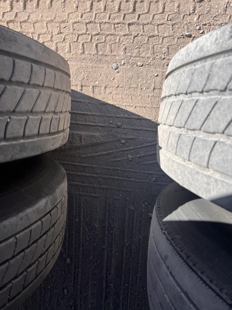 Trailer tires stacked on a utility van, tread patterns visible and dirt ground between them.