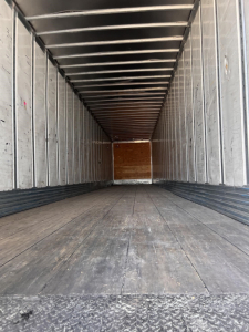 Trailer interior of a 2012 utility dry van showing metal walls, wooden floor, and rear entry with light at far end.
