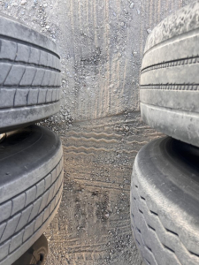 Trailer: dual stack of worn tires in a narrow space showing tread patterns and dirt. Center ground with marks.