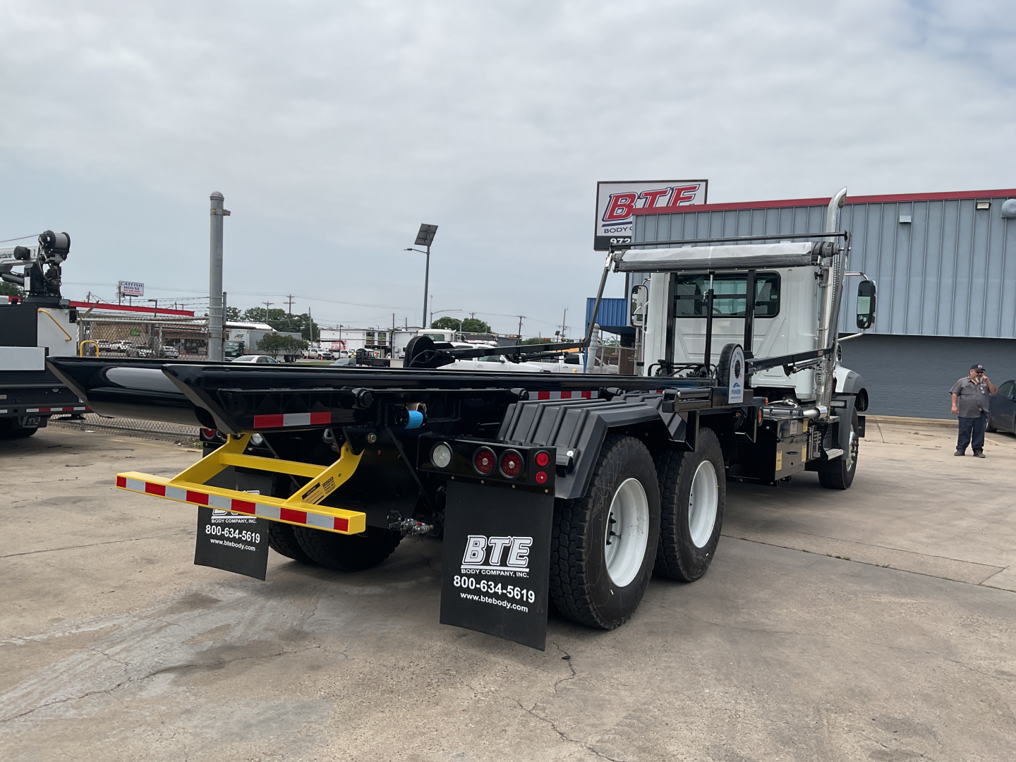 Mack GR64B roll-off truck rear view showing dual rear axles and rear bumper with BTE branding and contact numbers.