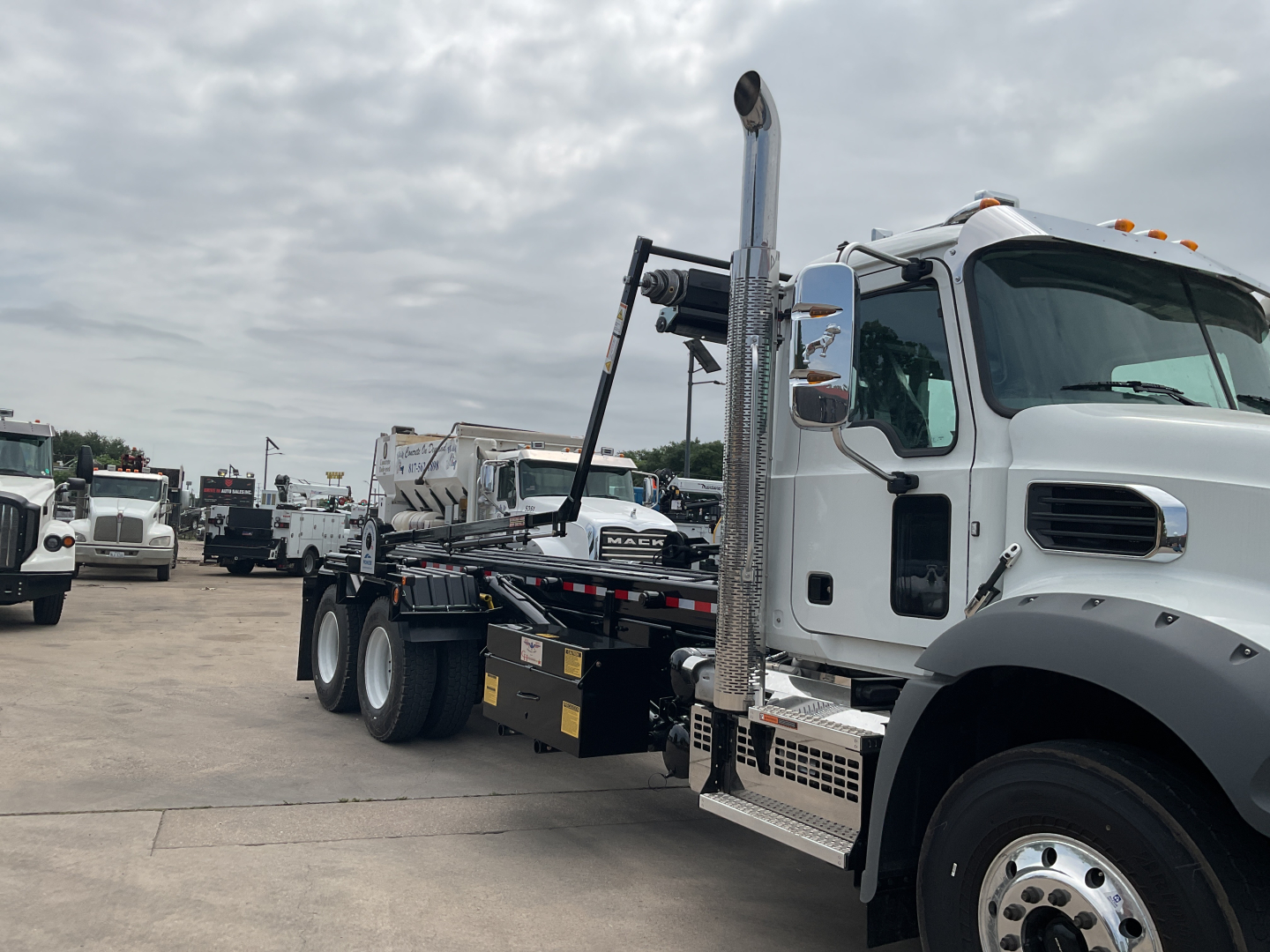 Mack GR64B roll-off truck side view showing cab, chrome exhaust stack, and rear loading platform.