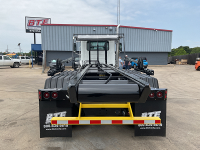 Mack GR64B roll-off truck rear view showing black chassis and yellow bumper, with BT&E logos on mud flaps and red/white reflective stripes.