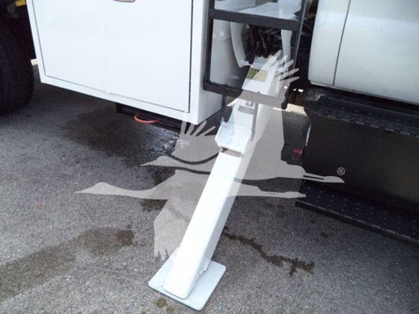 Ford F-750 bucket truck with stabilizing leg extended under side of cab; white hydraulic support beam and platform visible near driver door, underbody components and steps visible.