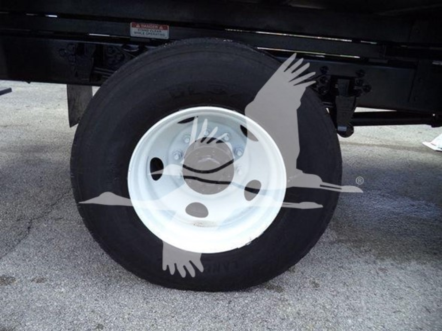 Truck wheel and tire showing white steel rim and black tire under Ford F750 bucket truck.