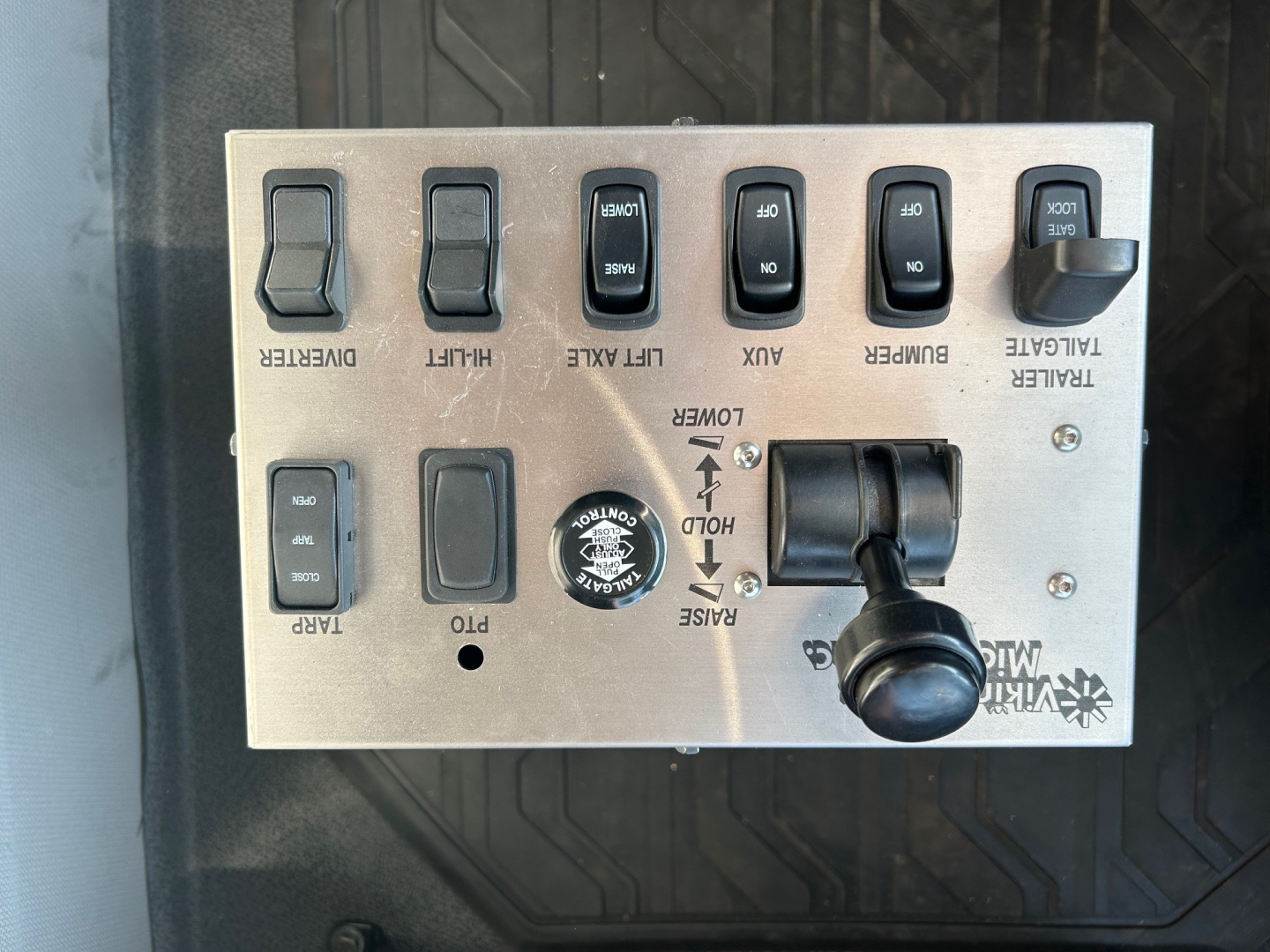 Panel of controls with switches labeled diesel, limiter, aux, power, purge, and engine start/stop levers on a Volvo dump truck dash; visible are multiple rocker switches and a round knob.