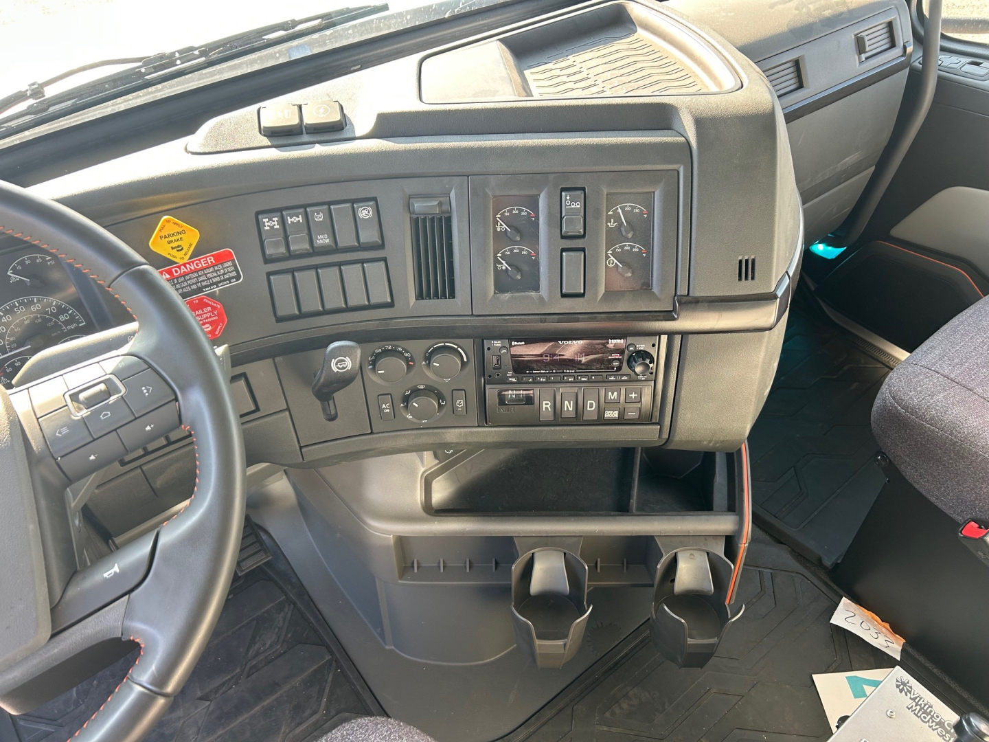 Dashboard of a Volvo VHD84F300 truck showing steering wheel, instrument cluster, climate controls, and gear selector with auxiliary cup holders.