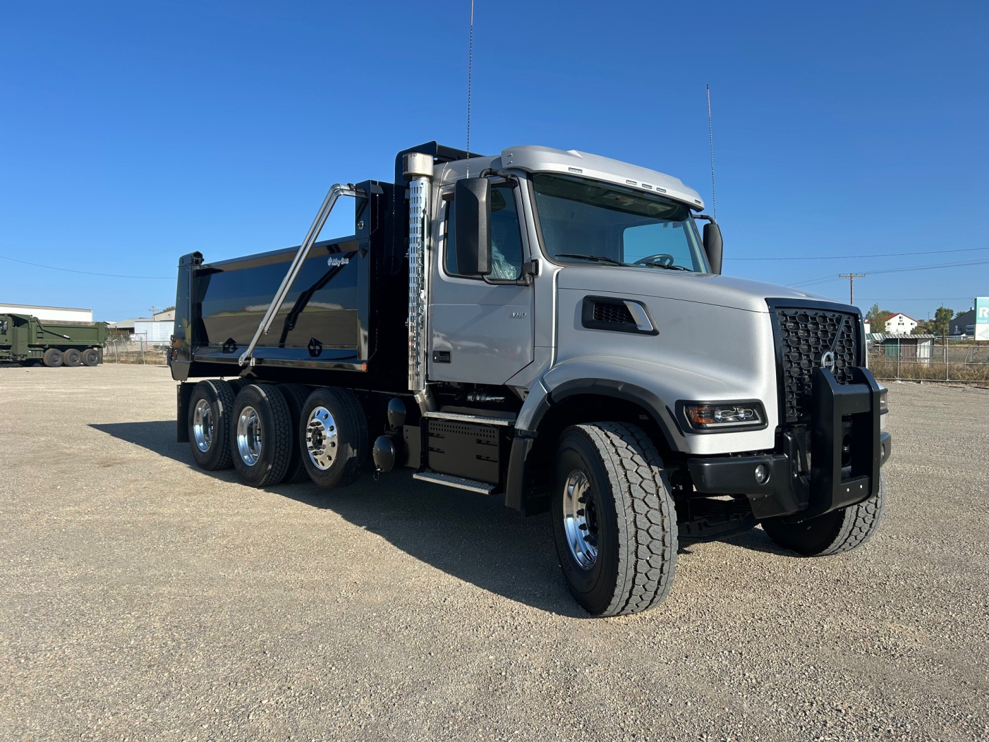 Volvo dump truck shown in side-front view with gray cab and black dump bed. Visible text on grille and windows not legible.