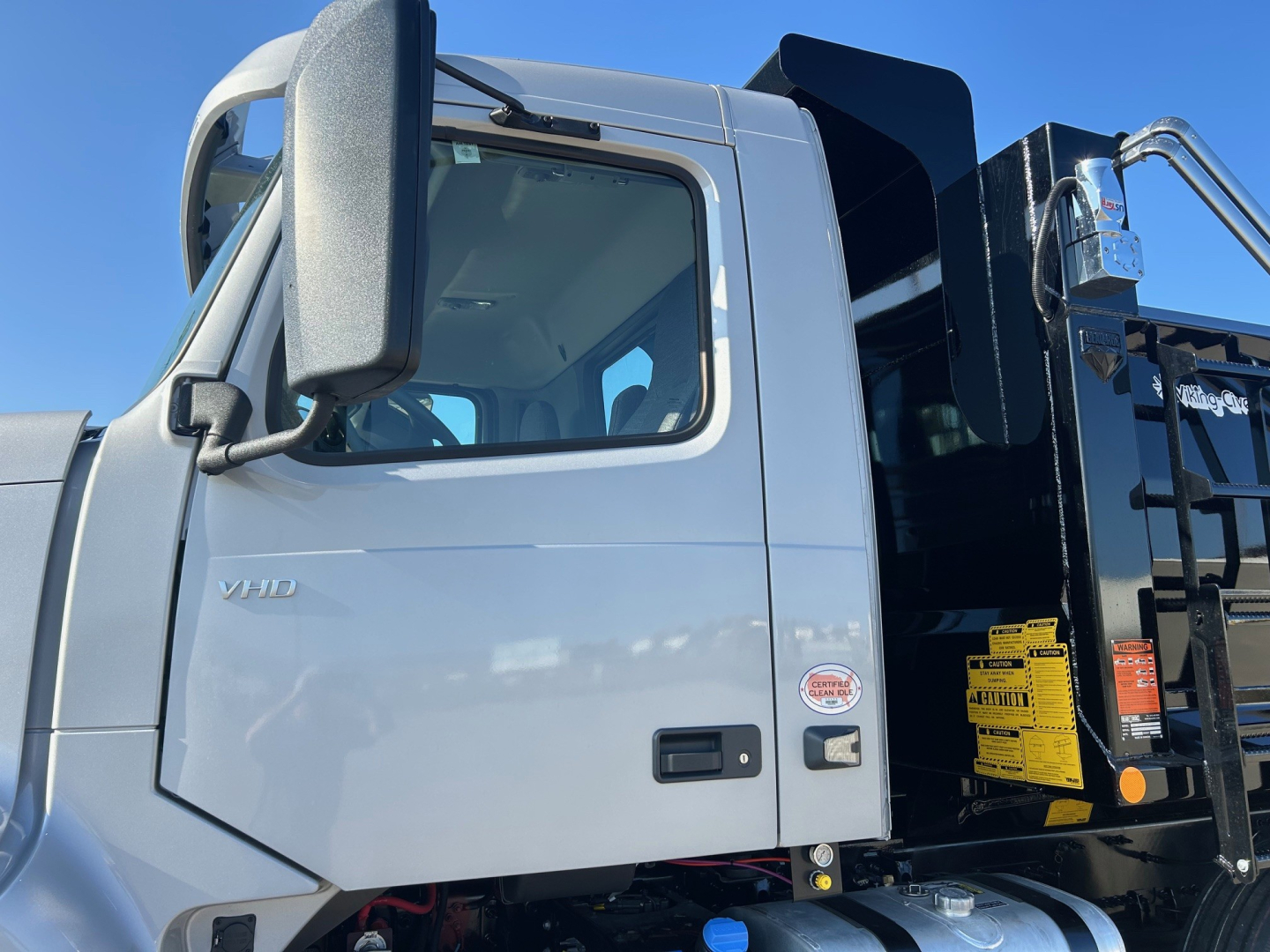 Volvo VHD84F300 dump truck cab side showing Volvo VHD badge and door area with side mirrors and metallic gray paint.