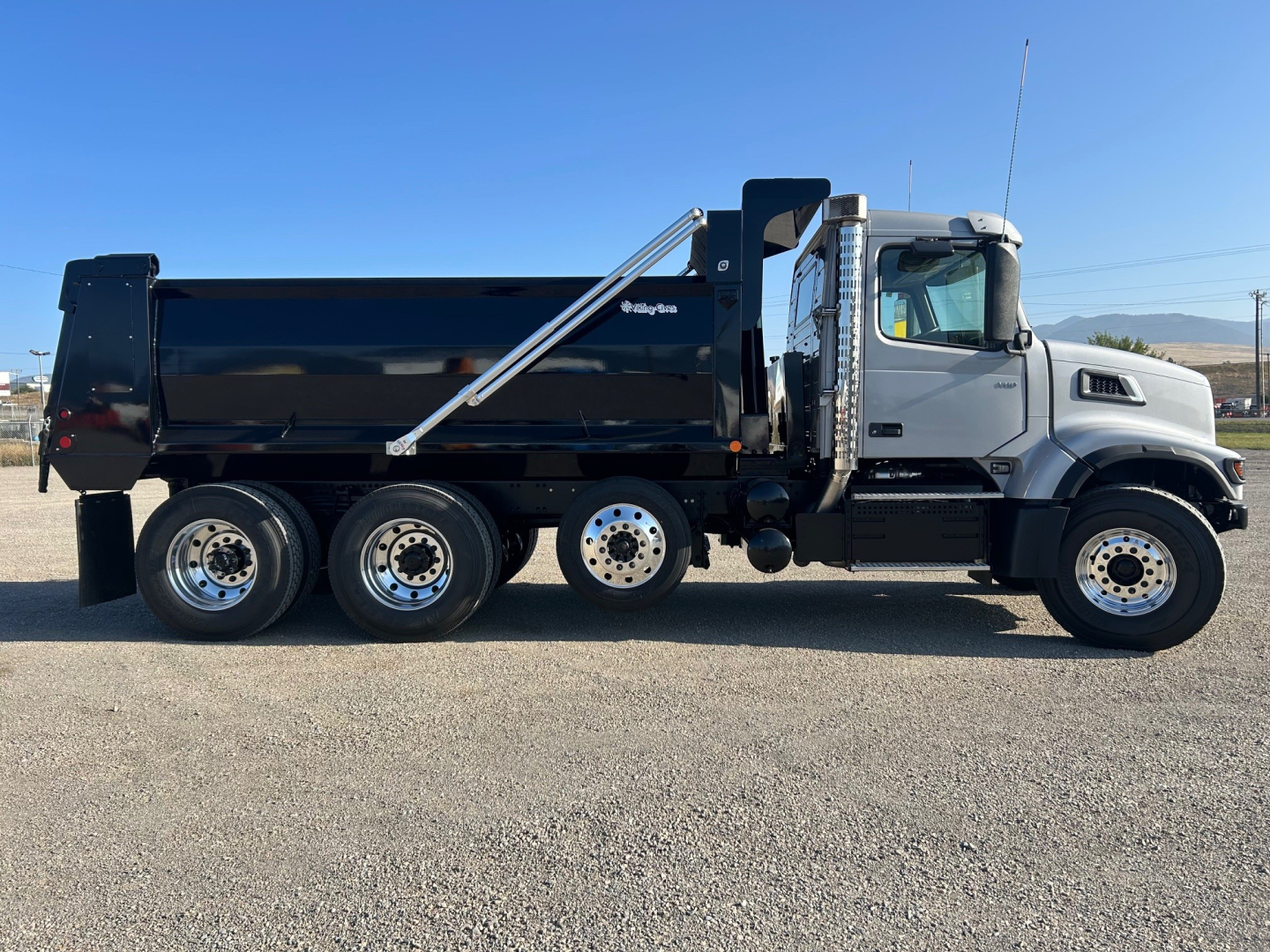 Side view of a new Volvo VHD84F300 dump truck showing a black dump body, chrome fuel tank area, and tandem rear axles with silver wheels.