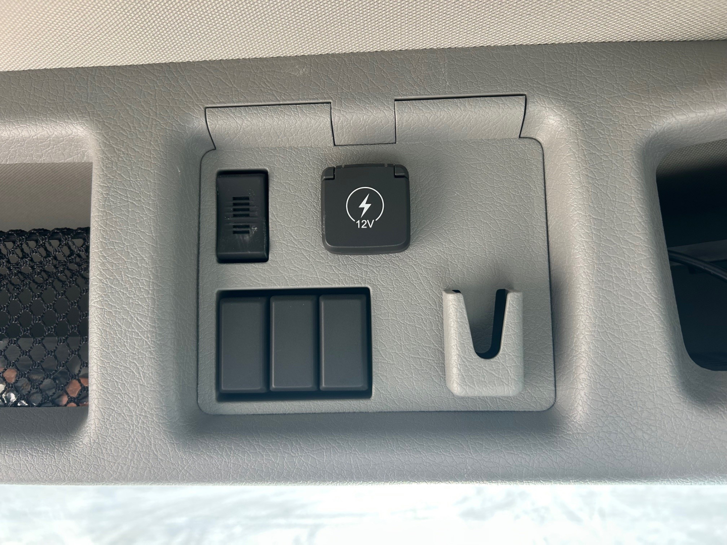 Interior console showing 12V power outlet, blank switch panel, and cup holder in Volvo VHD84F300 dump truck.