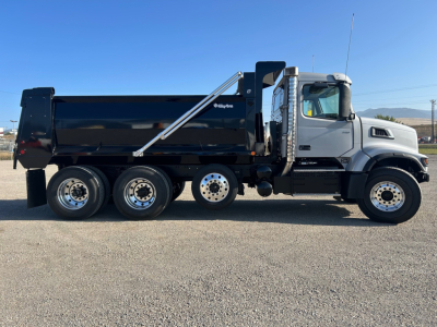 Side view of a new Volvo VHD84F300 dump truck showing a black dump body, chrome fuel tank area, and tandem rear axles with silver wheels.