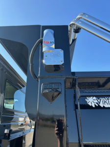 Volvo VHD84F300 truck component showing a blue and white hydraulic control valve with a black hose and chrome fittings mounted on a black chassis, with Volvo emblem on frame.