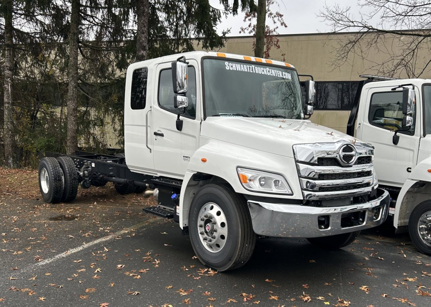 Hino L7 cab chassis truck in white, front three-quarter view with empty rear chassis, SCHWITZ TRUCKCENTER banner on windshield.