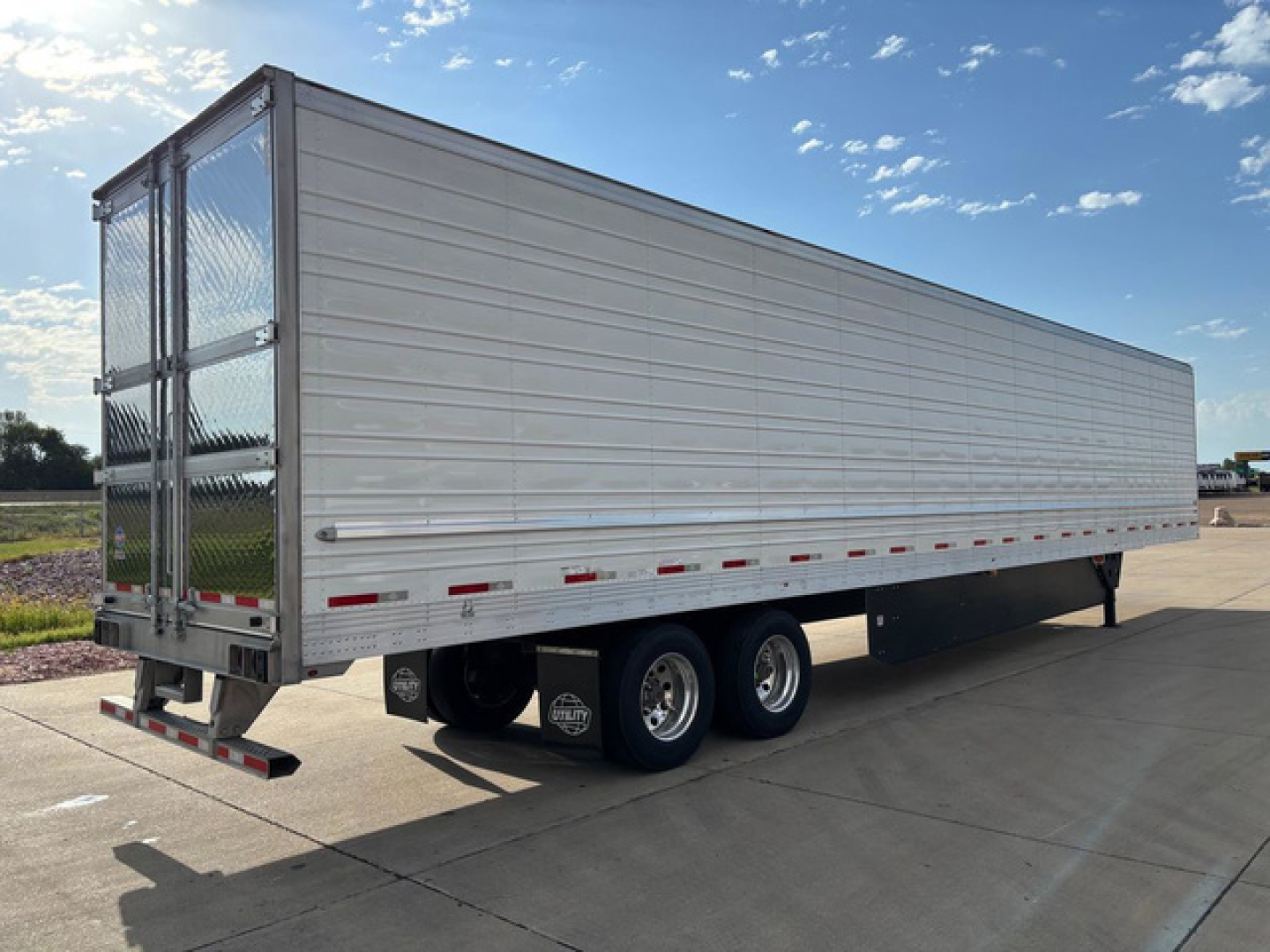 Utility reefer trailer side view showing aluminum box with rear doors and triple axle wheels.