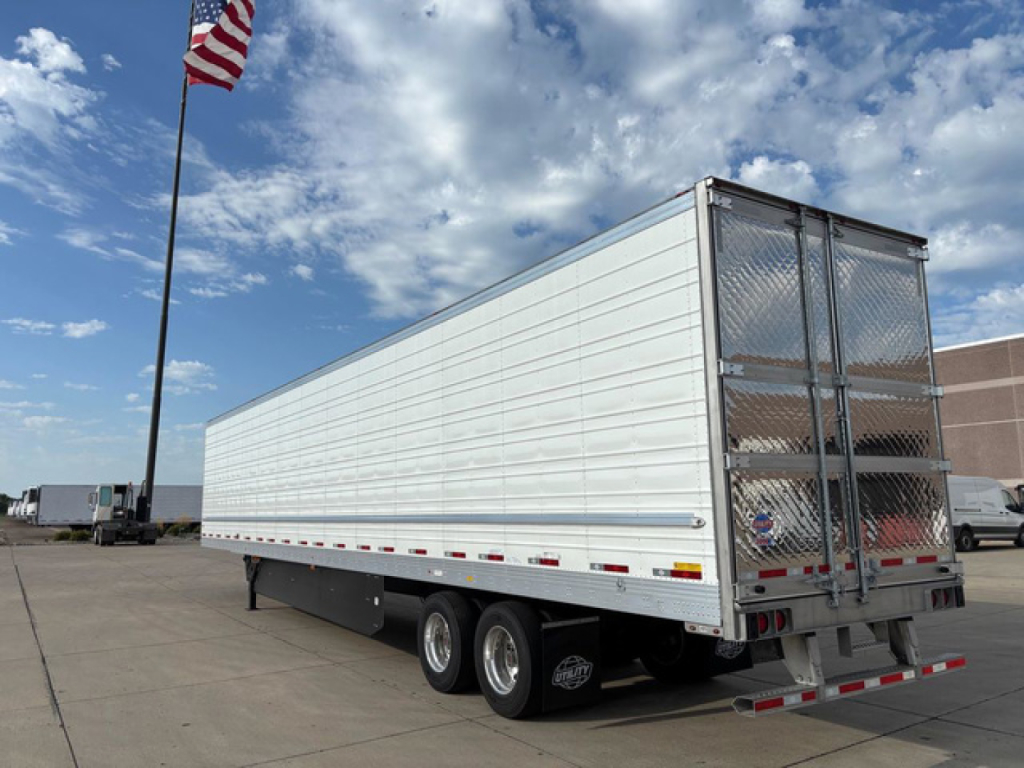 Utility reefer trailer side view with aluminum walls and dual rear doors, three-axle setup, undercarriage and reflective tape.
