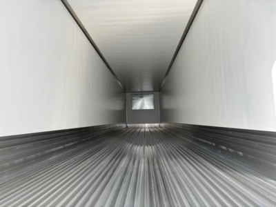 Trailer interior view showing long refrigerated cargo bed with ribbed metal floor and white walls, back wall small window opening.