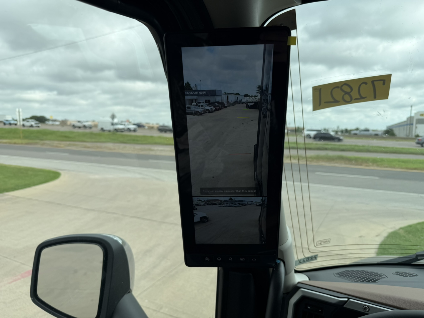 Interior view of a Mack truck cab with a central vertical screen mounted, dashboard area, windshield, and side view mirror visible.