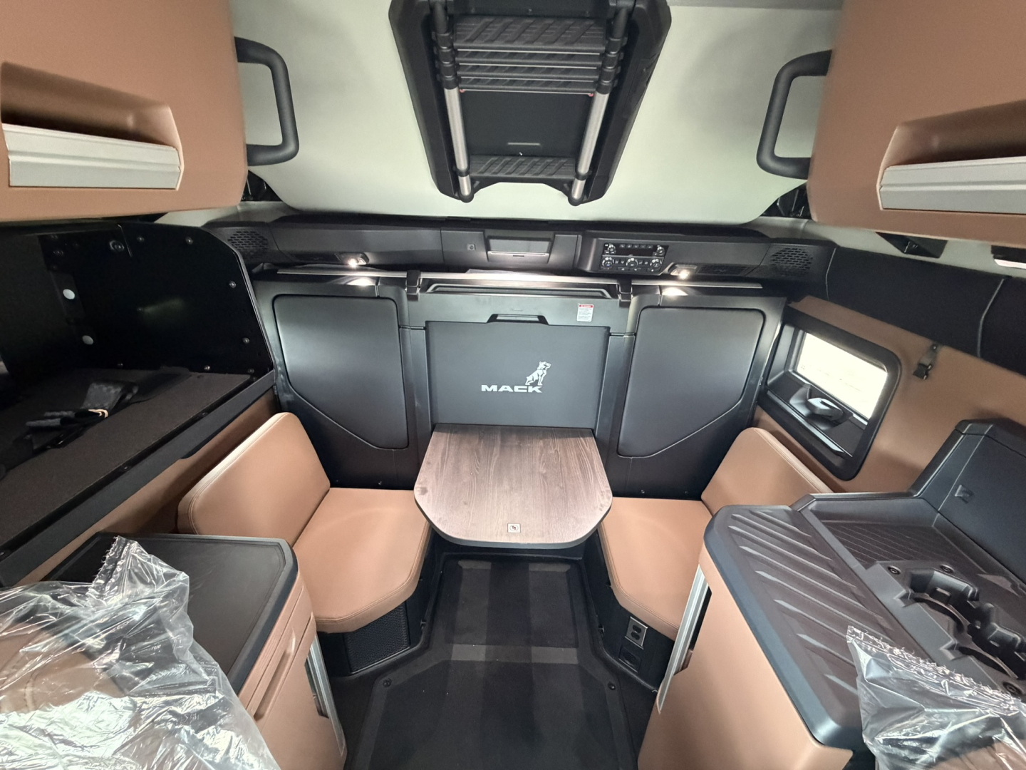 Mack PR64T76H truck interior cab with beige and black seating, table, and sleeper area.