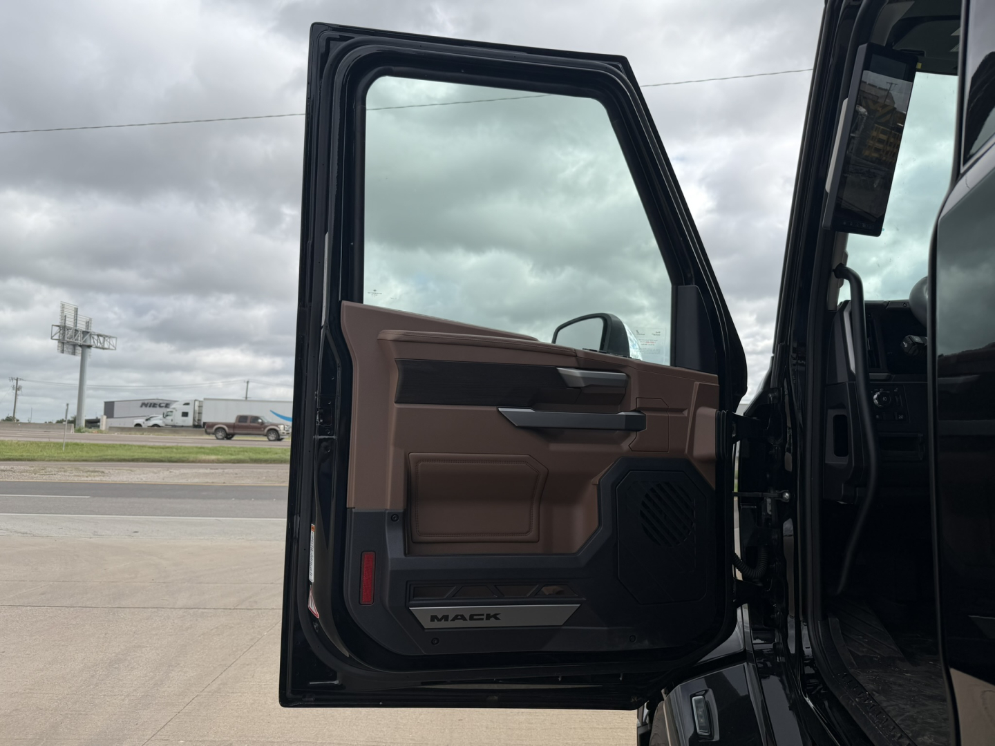 Truck door interior of a new 2027 Mack PR64T76H with brown and black cabin panel, open door showing Walker branding and control panel.