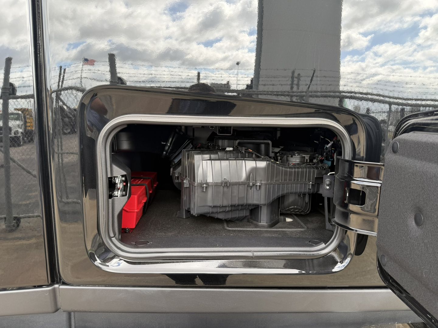 Truck cab door open showing engine or powertrain area with a silver component and red battery box in a sleeper cab; chrome trim around door opening.