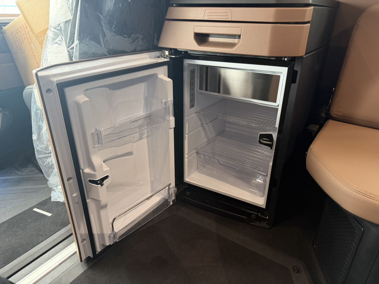 Mack PR64T76H sleeper cab interior showing a compact fridge/freezer with open door and empty shelves.