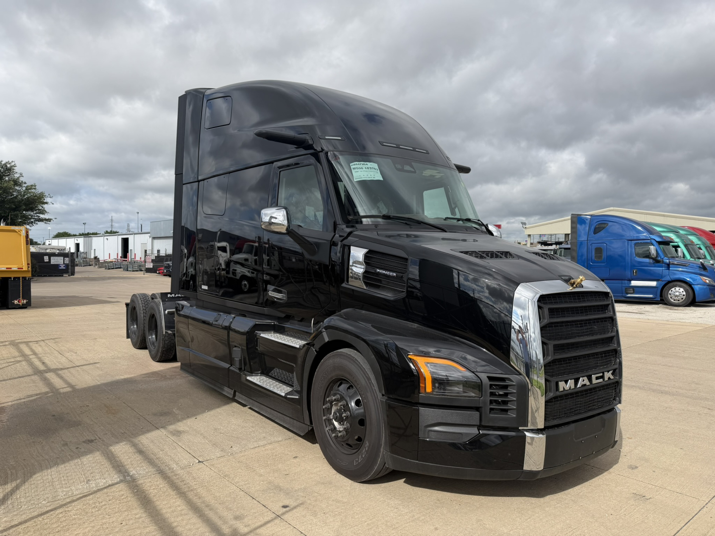 New Mack PR64T76H sleeper cab tractor in black, front and side view, with chrome grille and dual rear axles.