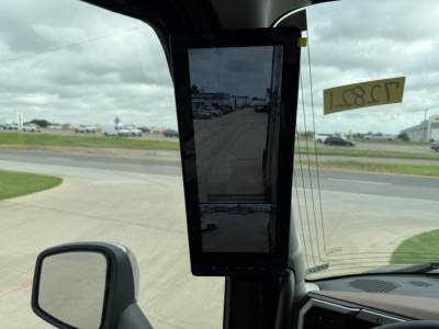 Interior view of a Mack truck cab with a central vertical screen mounted, dashboard area, windshield, and side view mirror visible.