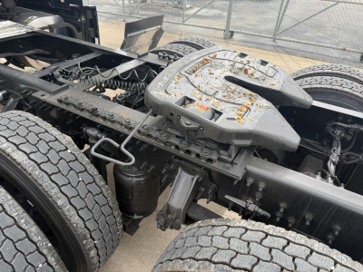 Mack PR64T76H tractor-trailer chassis showing dual rear axles and fifth wheel area with oily grime and spare parts; view of cabless tractor frame.