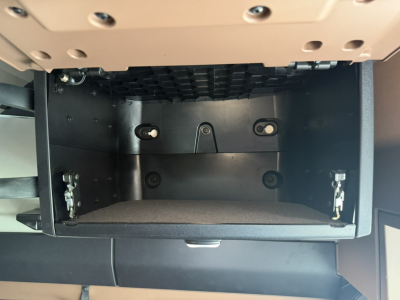 Dashboard storage compartment open under dash area with empty cubby and metal mounting points.