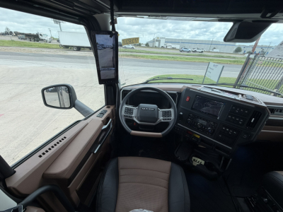 Cab interior of a Mack PR64T76H truck showing steering wheel, dashboard, center console, and side mirror.