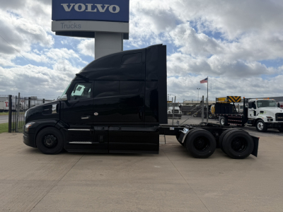Truck in front of Volvo dealer showing a black Mack PR64T76H tractor with a sleeper cab.