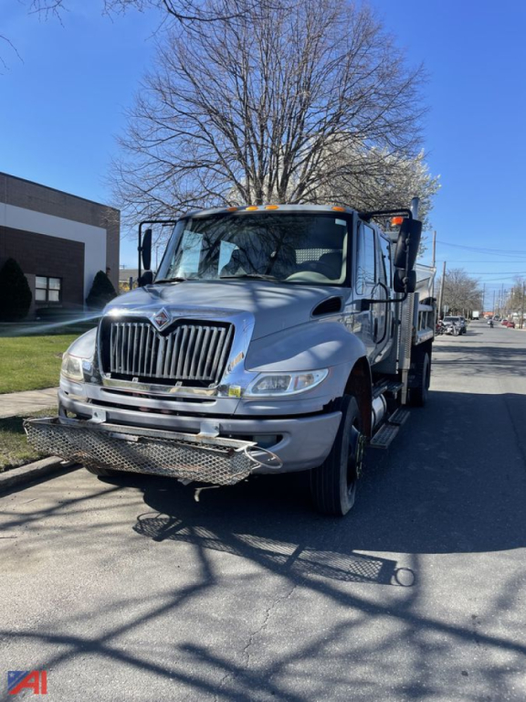 Front-left view of a 2012 International DuraStar 4300 crew cab dump truck showing front grille, bumper with skid plate, and dump bed hinge.