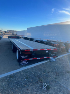 Trailer hitch showing 2025 Dura Haul steel drop deck trailer in-use with aluminum deck and dual axles, side markings and rear lights visible.