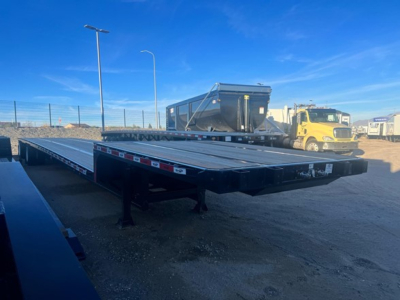 Drop deck trailer in-service showing steel flatbed with black frame and reflective tape along side.