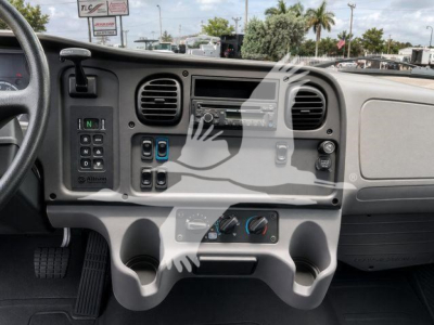 Interior dash of a crane cab showing steering column, gear selector, climate controls, cup holders, and radio in a gray dashboard.