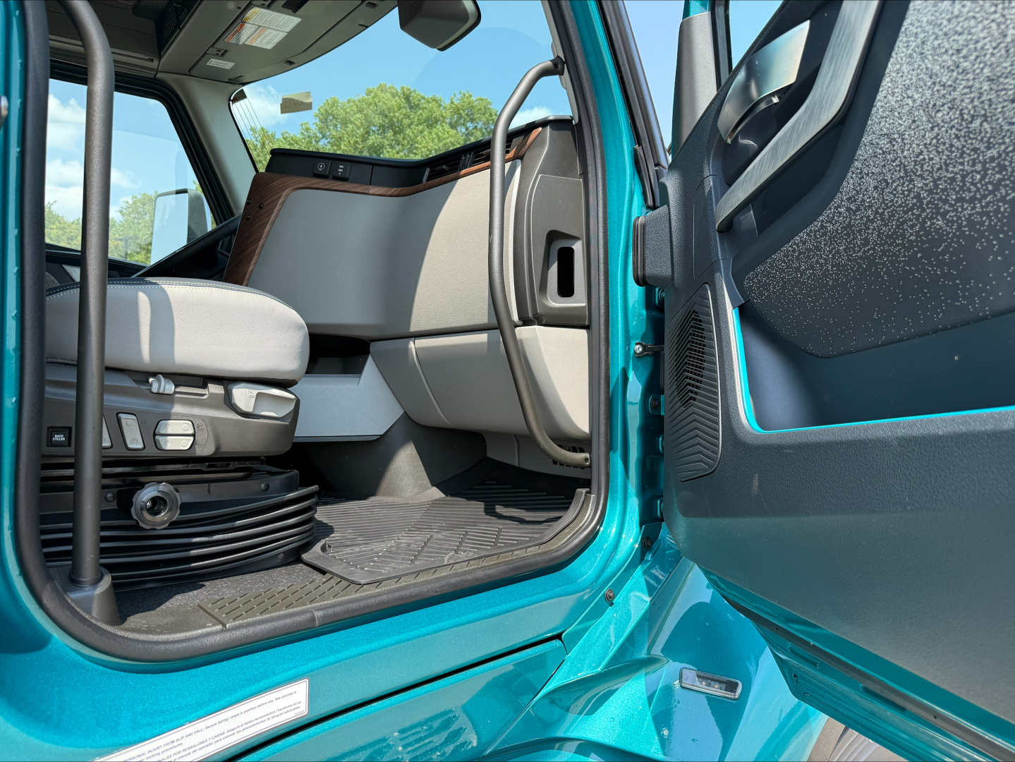Cabin interior of a Volvo VNL truck with doorway open, showing driver seat, entry step, and part of the sleeper area.