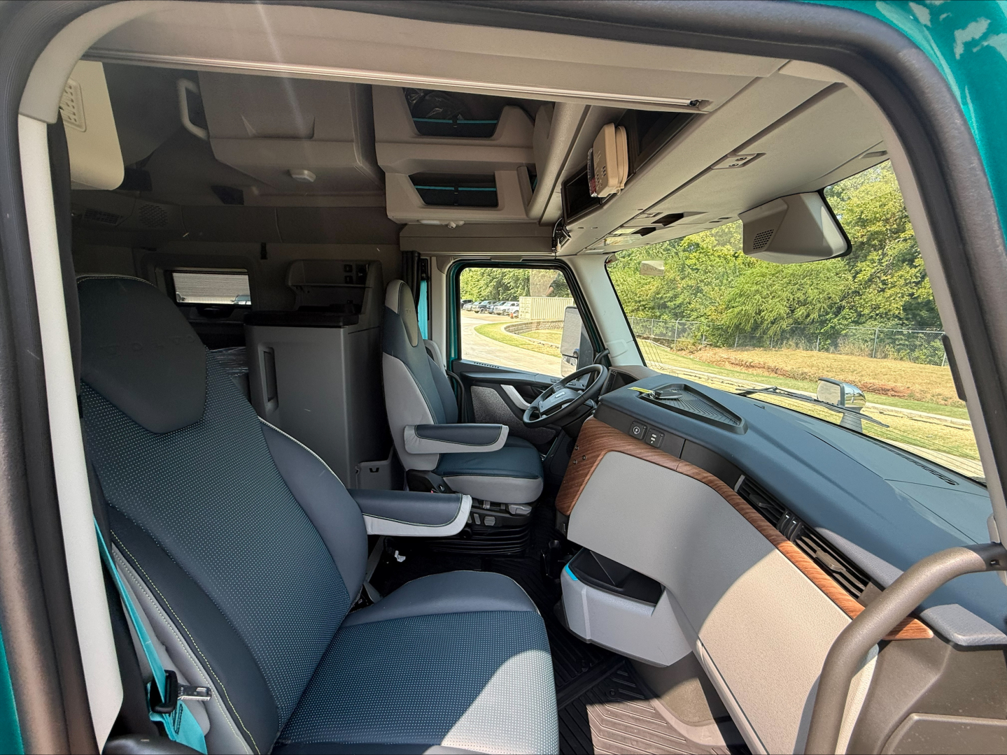 Cab interior of a new Volvo VNL64T860 with gray seats, modern dashboard, steering wheel, and overhead storage. Passenger seat swiveled; view through open door.